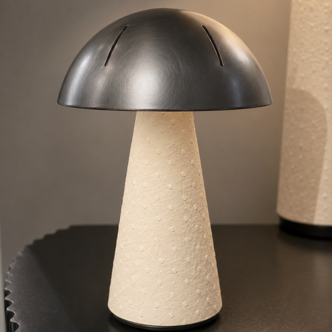 A mushroom-shaped table lamp with a matte black dome-shaped shade and a textured cream-colored tapered base, shown on a dark tabletop with a softly blurred background.