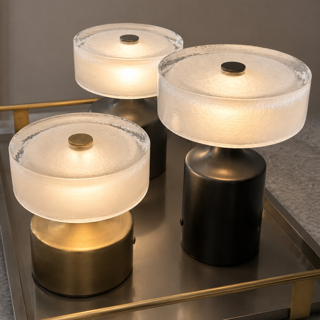 Three modern table lamps with frosted circular shades and cylindrical bases, arranged on a metallic tray against a neutral gray background.