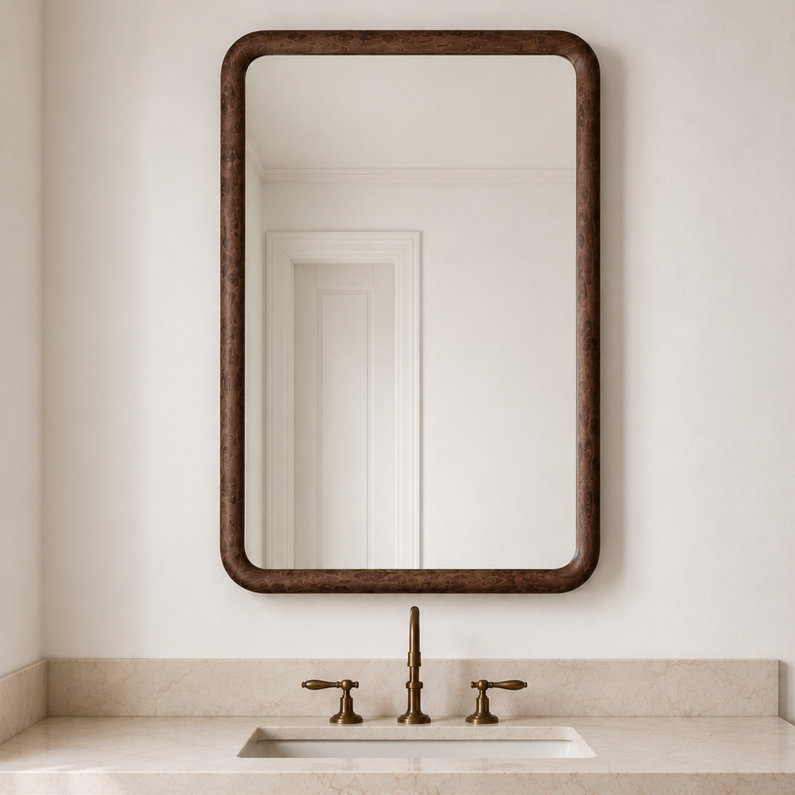 A rectangular wall mirror with a dark brown textured frame, mounted on a white bathroom wall above a vanity with a marble countertop and brass faucet.