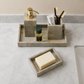 A marble bathroom organizer tray set on a white marble countertop, holding a gold-tone soap dispenser, toothbrushes, a small perfume bottle, and a bar of soap in a separate tray.