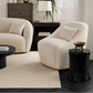 A styled living room featuring two cream boucle armchairs, a dark wood sideboard with a gold-framed mirror, a potted palm, and a textured cream rug on dark wood floors.