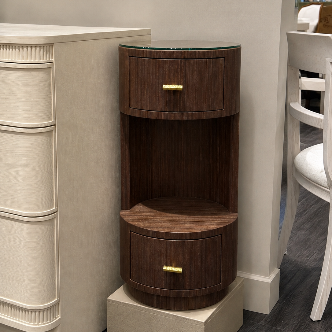 A dark brown wooden side table with two drawers and a glass top, styled in a modern home interior next to a cream-colored cabinet.