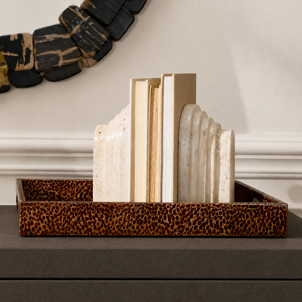 A decorative tray with a brown and black leopard print pattern holds a set of cream and beige stone bookends and books against an indoor wall backdrop.