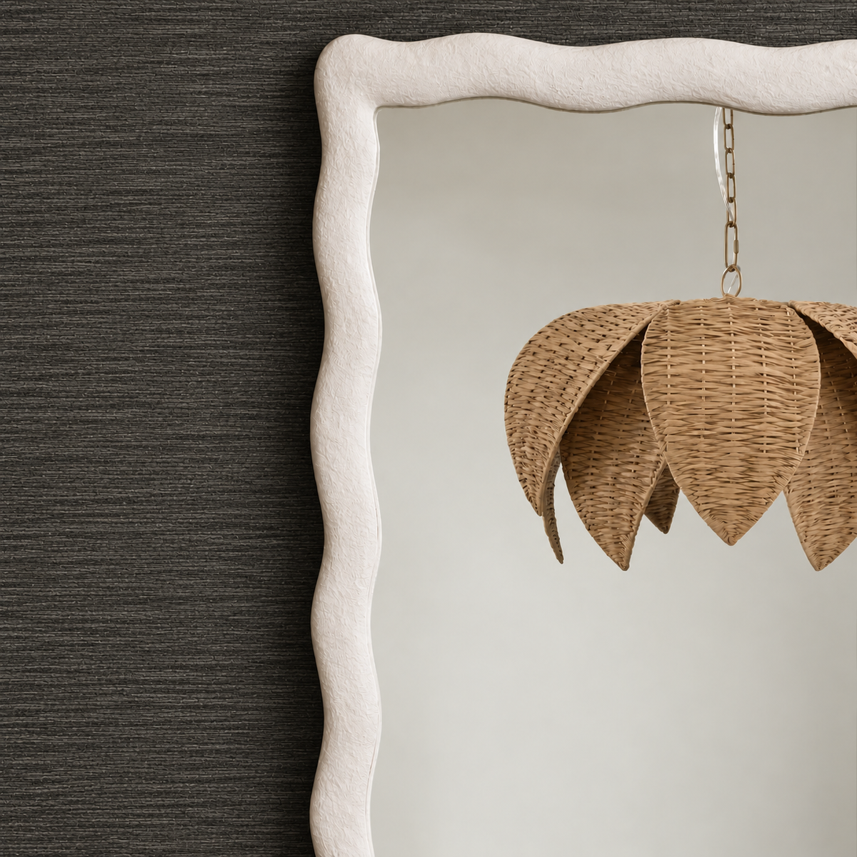 A close-up of a decorative wall mirror with a thick, wavy off-white frame, reflecting a woven natural rattan pendant light against a dark textured wall.
