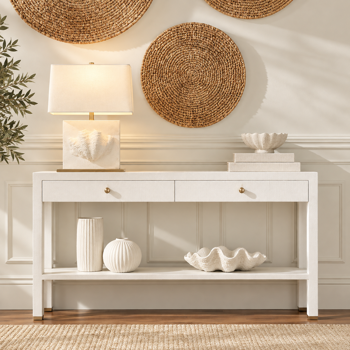 A white console table with two drawers and an open lower shelf, styled in a bright, neutral room with decorative vases, a lamp, wall art, and a plant.