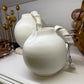 White ceramic teapots on a white surface with decorative elements in the background.