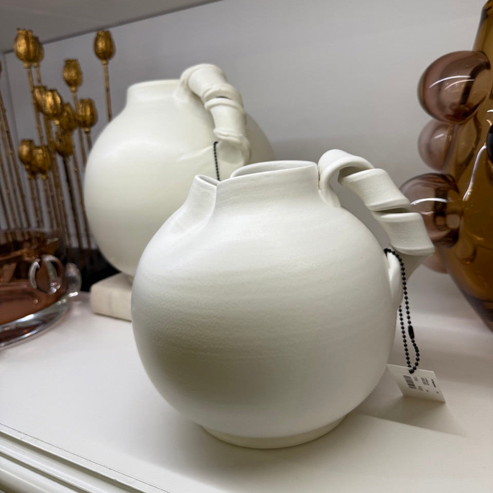 White ceramic teapots on a white surface with decorative elements in the background.