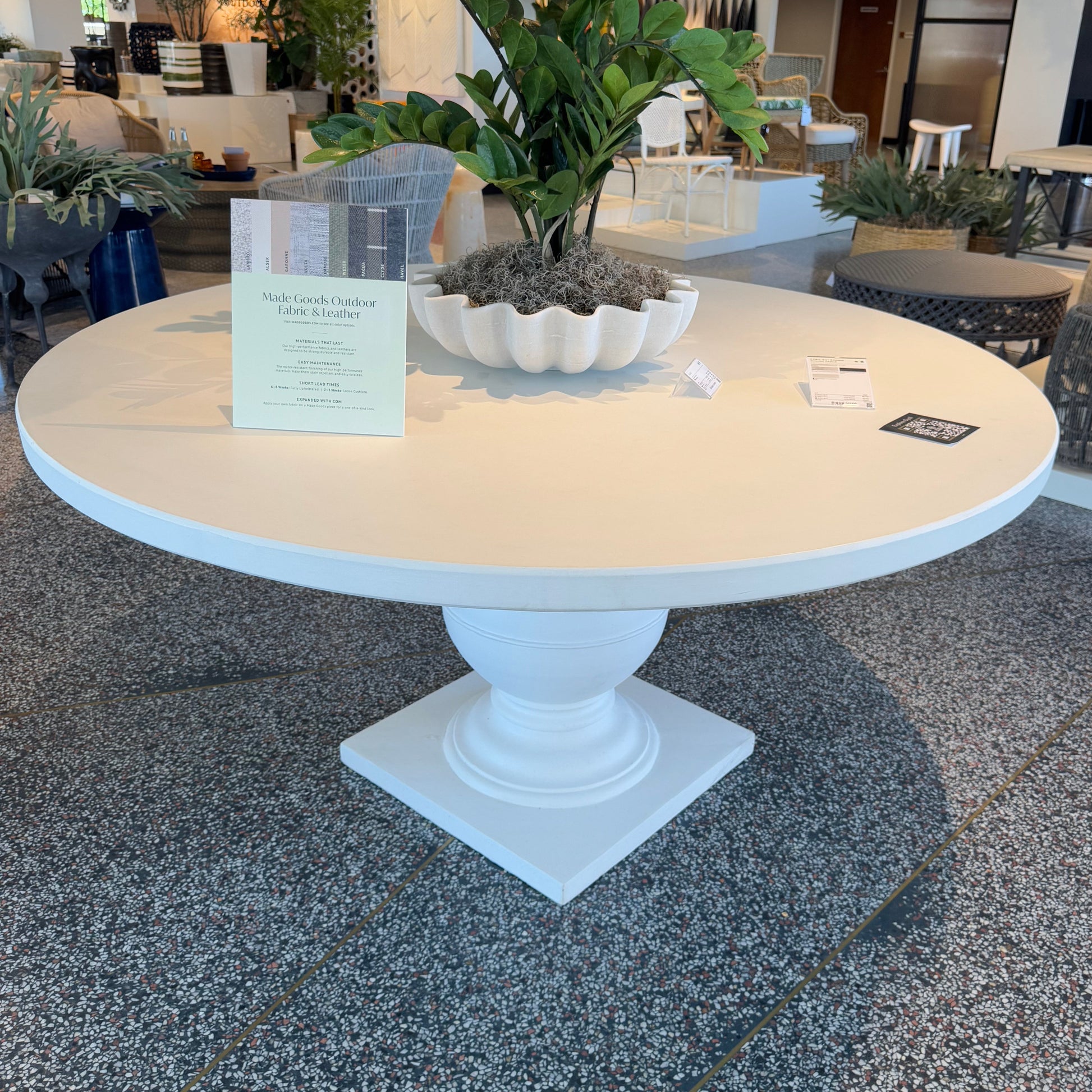 Round white table with a plant on a gray floor in an indoor setting