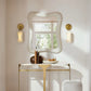 Decorative wall mirror with two sconces on a white wall.