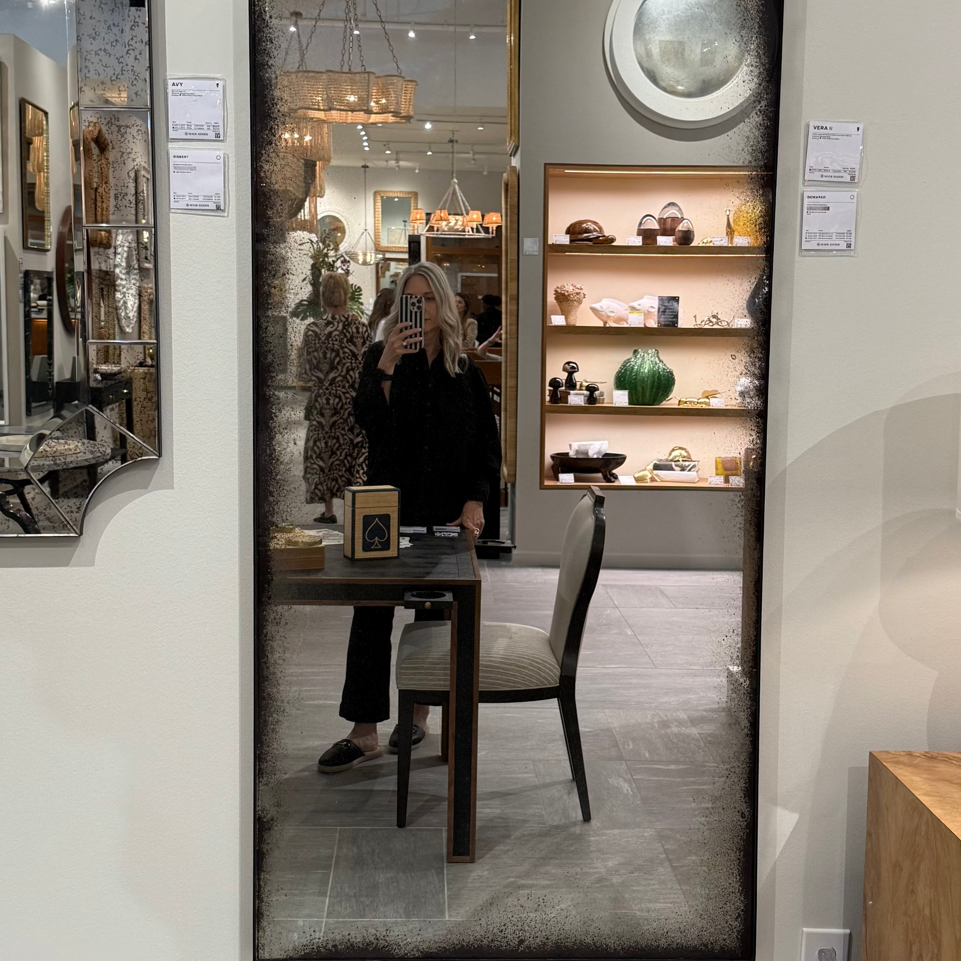 Person taking a mirror selfie in a room with decorative items on shelves.