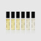 Six small perfume bottles with black caps on a light gray background