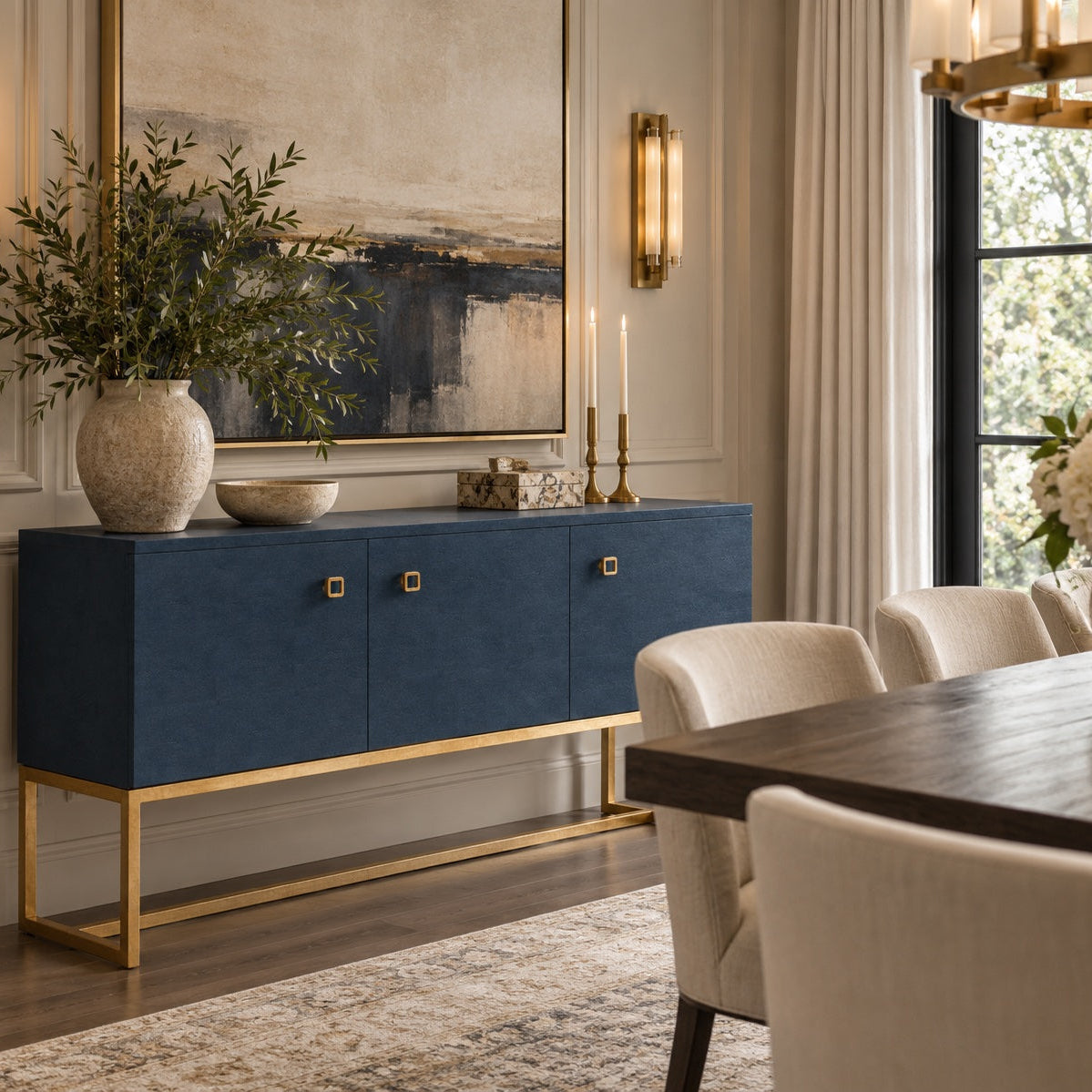 A navy blue sideboard cabinet with a gold metal frame and gold square knobs, styled in a modern dining room setting.