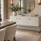 A modern white sideboard cabinet with a silver metal frame in a styled dining room setting, decorated with a vase of greenery, books, and candles.