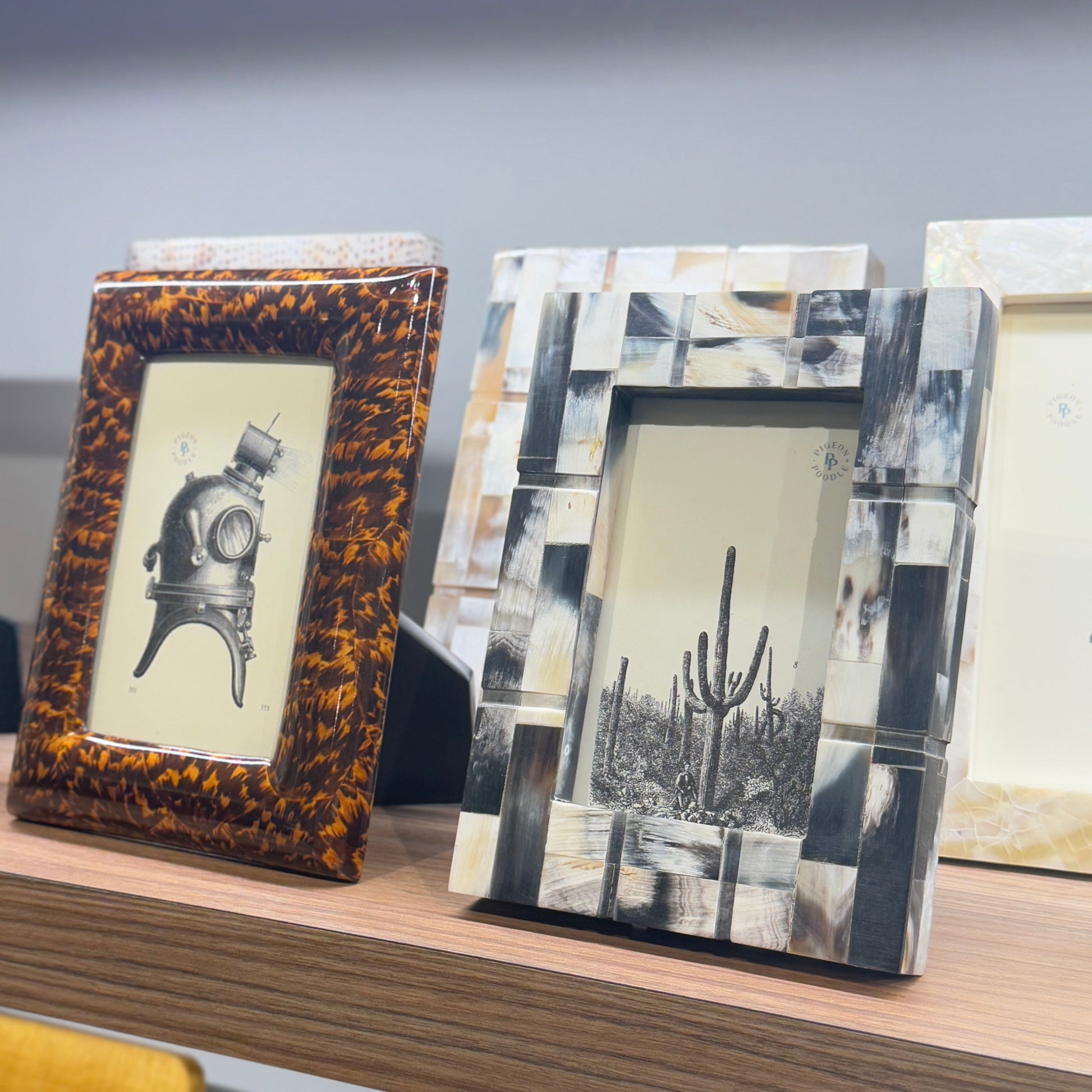 Three decorative picture frames on a shelf with a neutral background