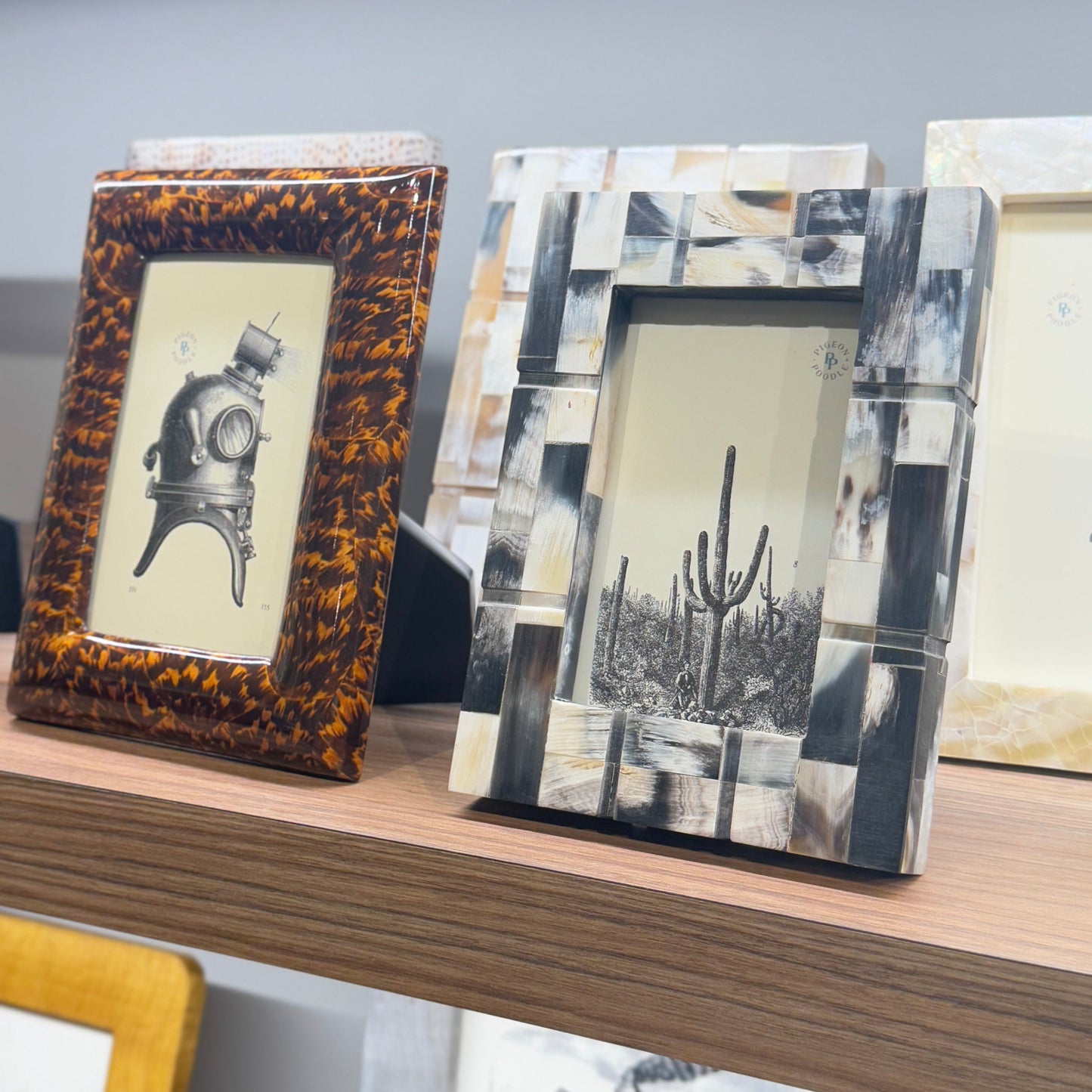 Three decorative picture frames on a shelf with a neutral background