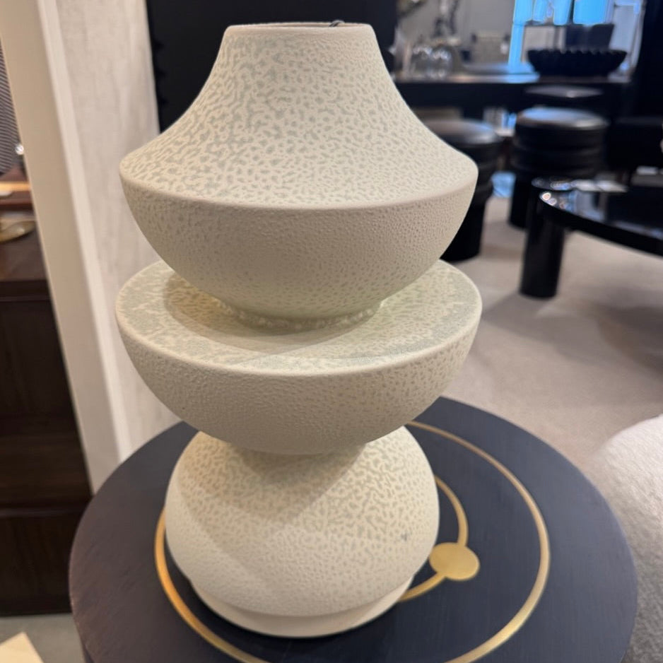 Two-tiered textured vase on a dark surface with a blurred indoor setting