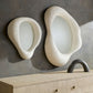 Two modern wall mirrors with a textured, organic design on a gray wall.