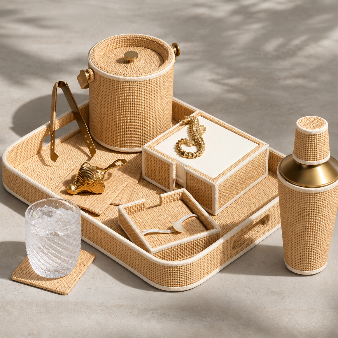 A coordinated bar and storage set arranged on a tray, including a woven cylindrical bucket with lid, a cocktail shaker, a small glass, gold-toned accessories, and a jewelry box, photographed on a neutral surface with soft shadows.