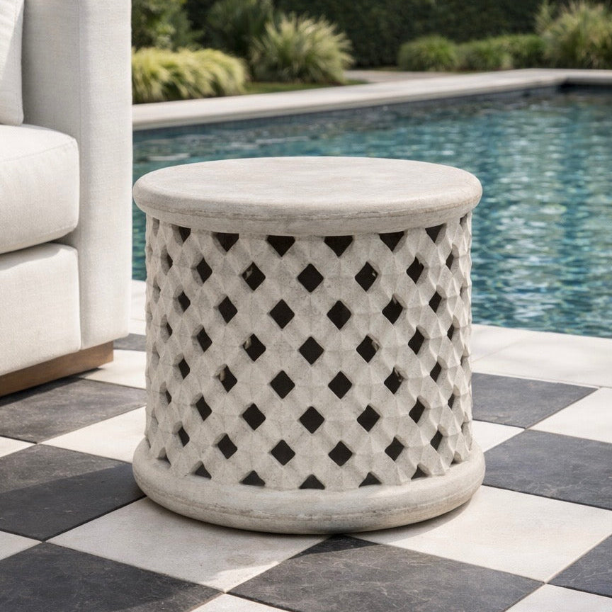 Decorative outdoor side table with lattice pattern on a checkered patio by a pool.