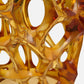 Close-up of a translucent amber-gold sculptural object with an organic, web-like open structure against a white background.