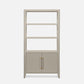 A tall, narrow bookcase with four open shelves on the upper portion and two cabinet doors on the lower portion, finished in a light warm gray or greige tone with slim gold-toned vertical handles, shown on a plain light gray background.