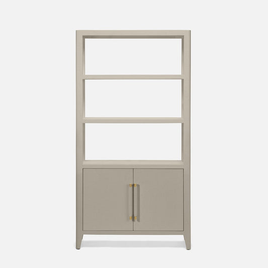 A tall, narrow bookcase with four open shelves on the upper portion and two cabinet doors on the lower portion, finished in a light warm gray or greige tone with slim gold-toned vertical handles, shown on a plain light gray background.