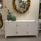 Decorative mirror with gold leaf design above a white cabinet in an interior setting.