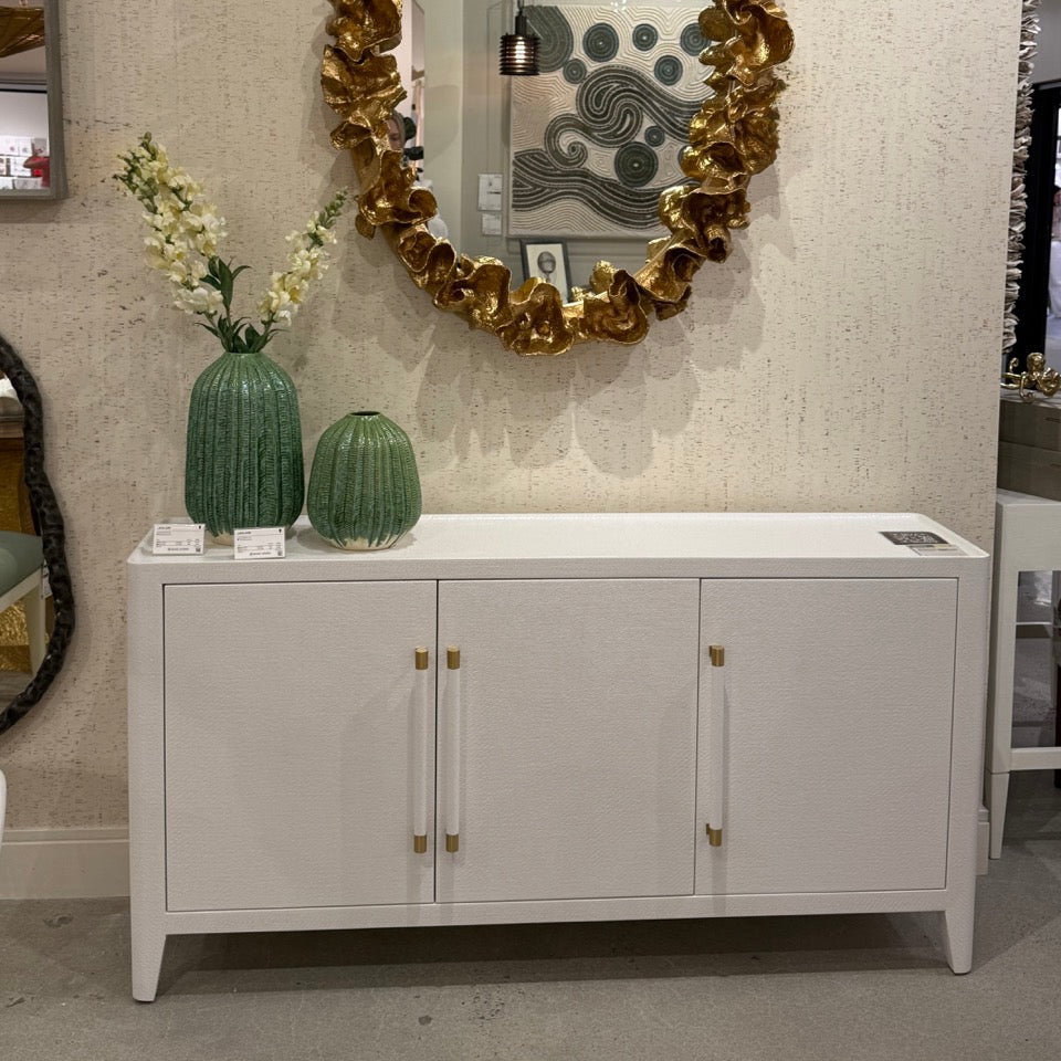 Decorative mirror with gold leaf design above a white cabinet in an interior setting.
