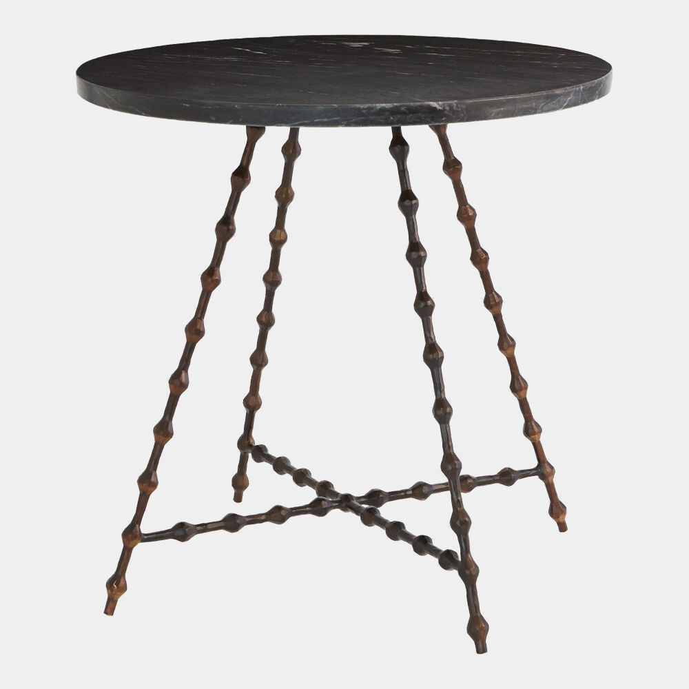 A round dark stone side table with a black marble top and a unique bronze-finished metal base featuring twisted, beaded legs and a crisscross lower support.