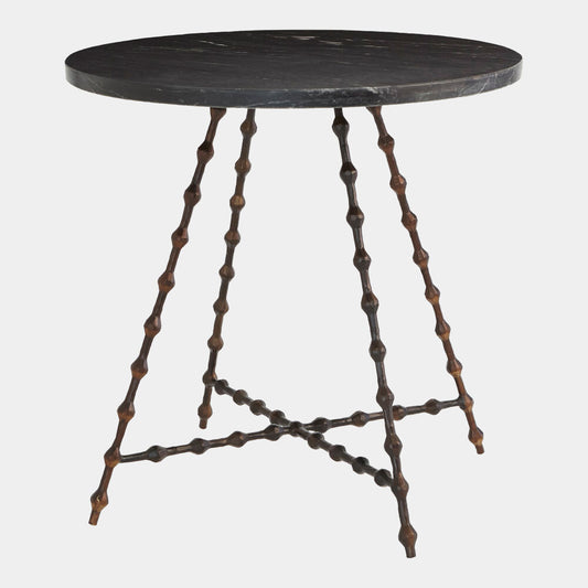 A round dark stone side table with a black marble top and a unique bronze-finished metal base featuring twisted, beaded legs and a crisscross lower support.