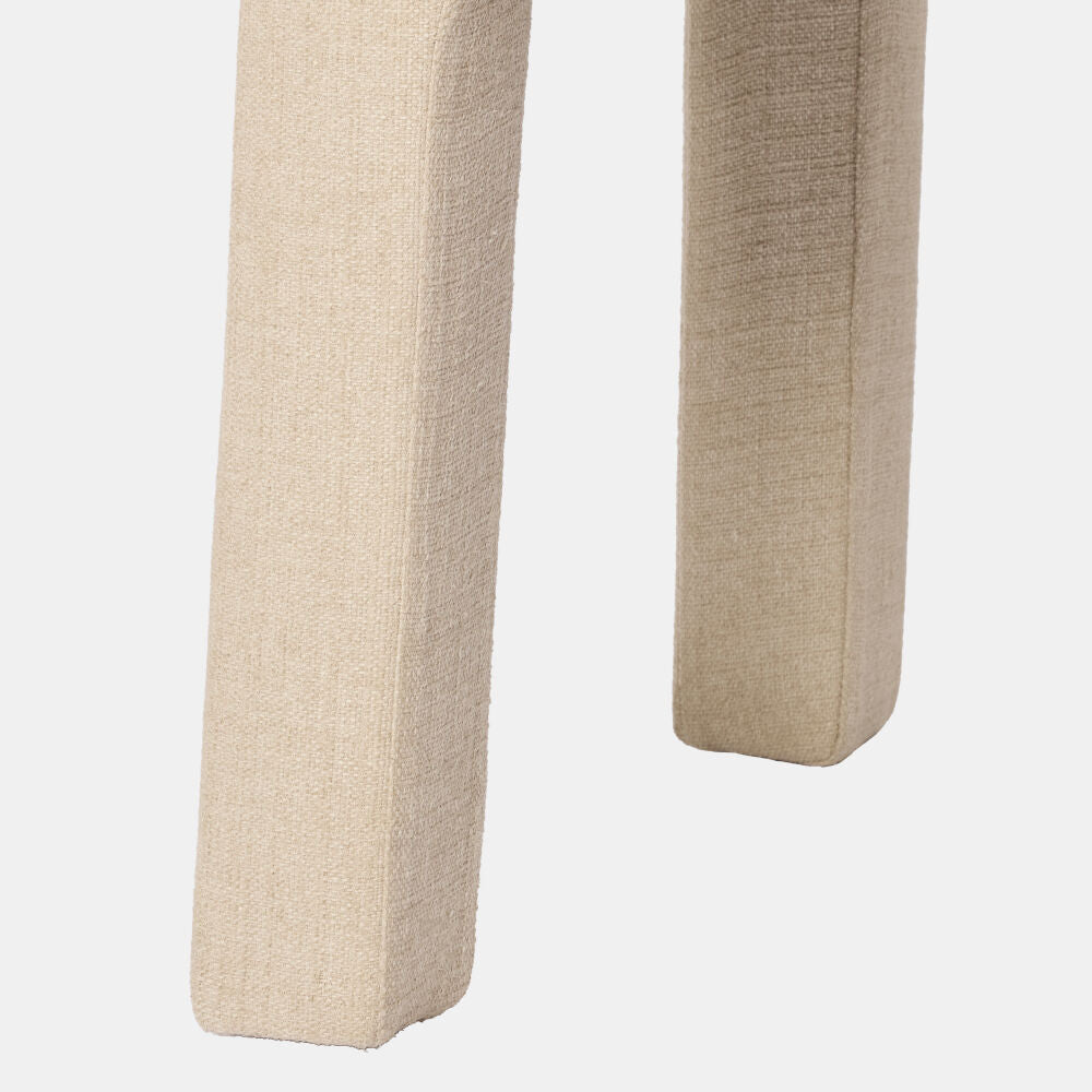 Close-up of the upholstered legs of a light beige fabric chair or stool against a plain light gray background.