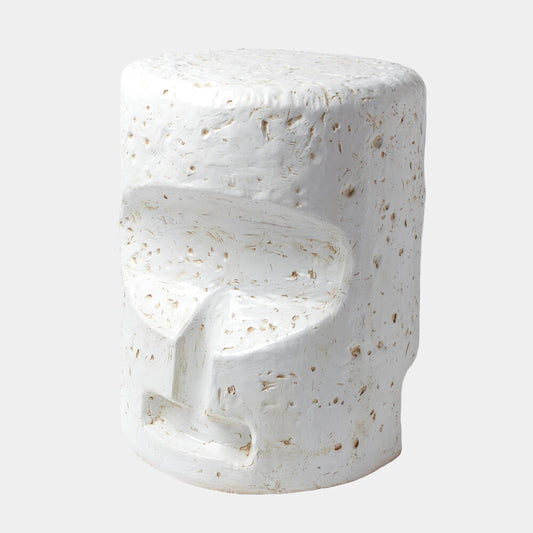 A modern sculptural side stool with a textured, organic shape resembling a stylized face, finished in white with natural beige stone flecks, set against a light gray background.