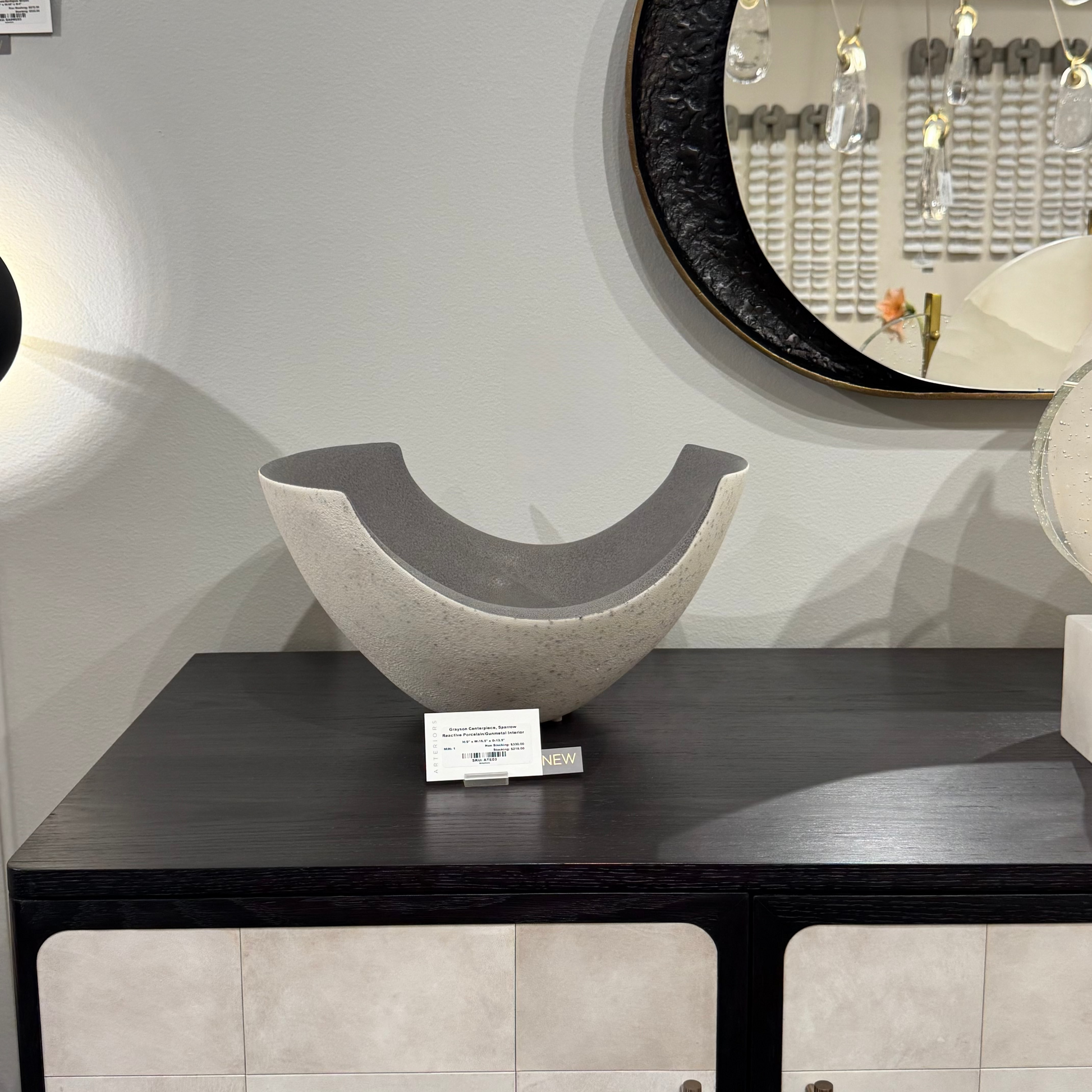 Decorative bowl on a dark wooden table with a round mirror in the background