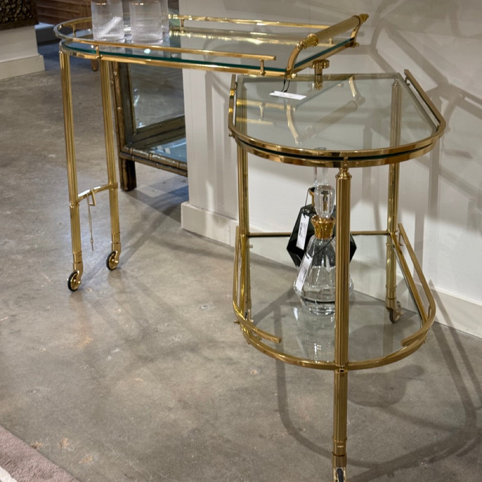 Set of two gold-framed glass tables on a concrete floor.