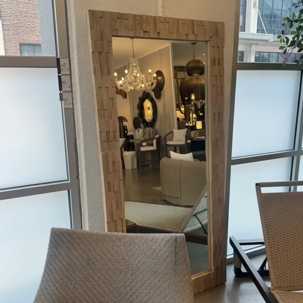 Large decorative mirror with a geometric frame in a room with chairs and a chandelier.