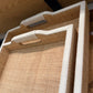 Woven tray with beige woven surface and white handles on a wooden surface.