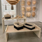 Two woven storage baskets with black and natural beige lower sections are displayed on a light wood bench in a modern home decor showroom.
