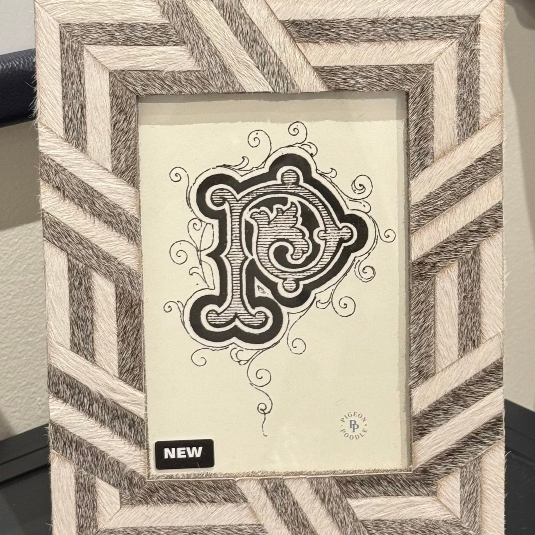 Decorative picture frame with geometric pattern and central monogram design on a plain background.