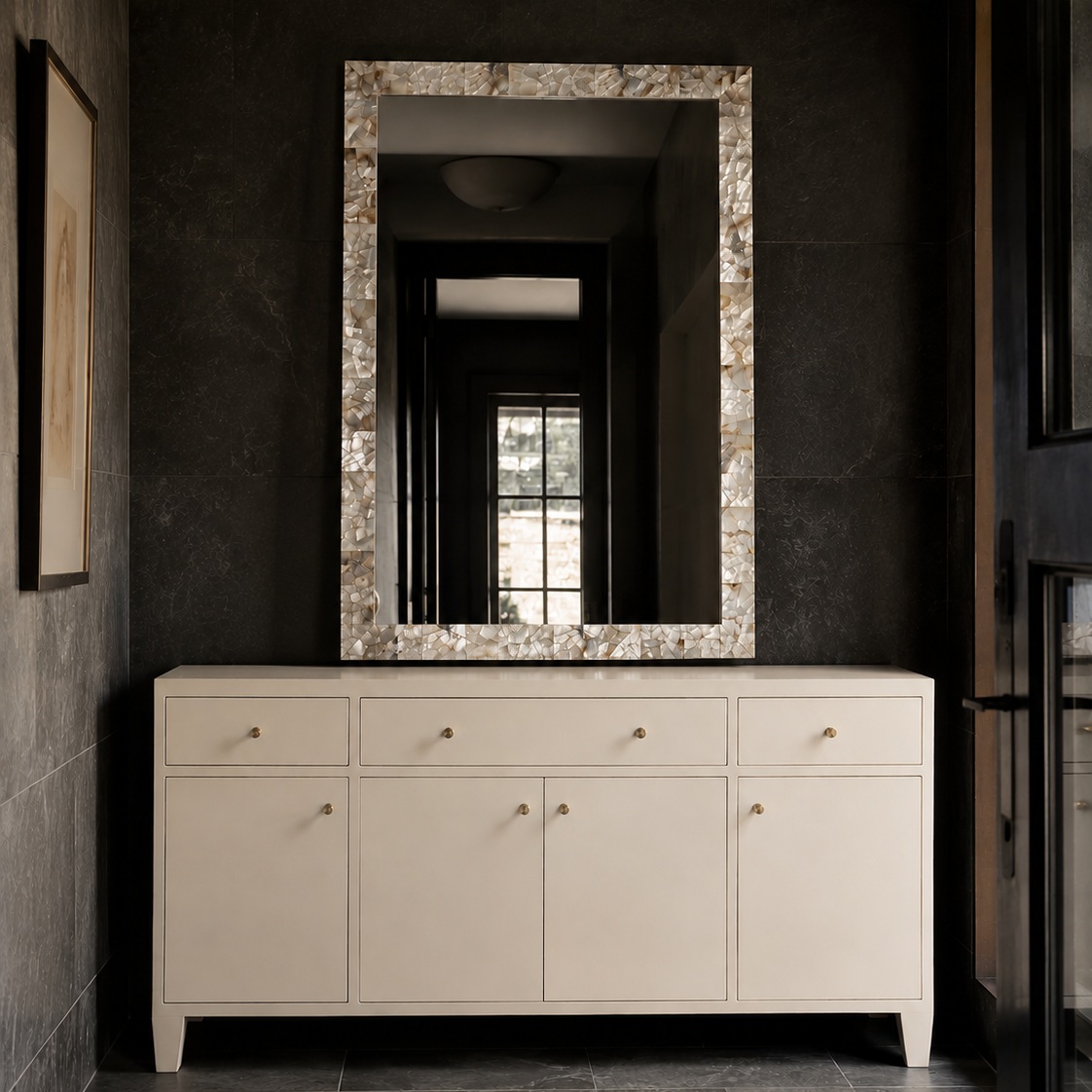 A cream-colored wooden console cabinet with a large rectangular mirror featuring a textured, metallic-look border, set against a dark charcoal tiled wall.