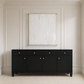 A black wooden sideboard or credenza with five drawers and three cabinet doors, each featuring a small round gold pull, set against a cream paneled wall with a framed abstract print above.