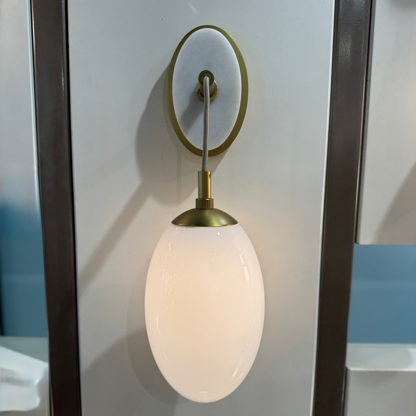 Wall-mounted light fixture with white glass shade and brass fixture on a neutral background