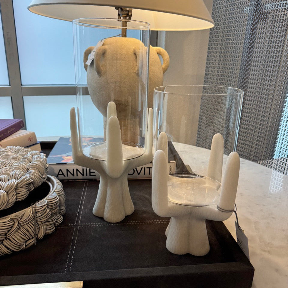 White ceramic candle holders on a dark surface with a lamp and books in the background.