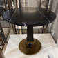 Round black marble table on a white marble base with a textured wall in the background