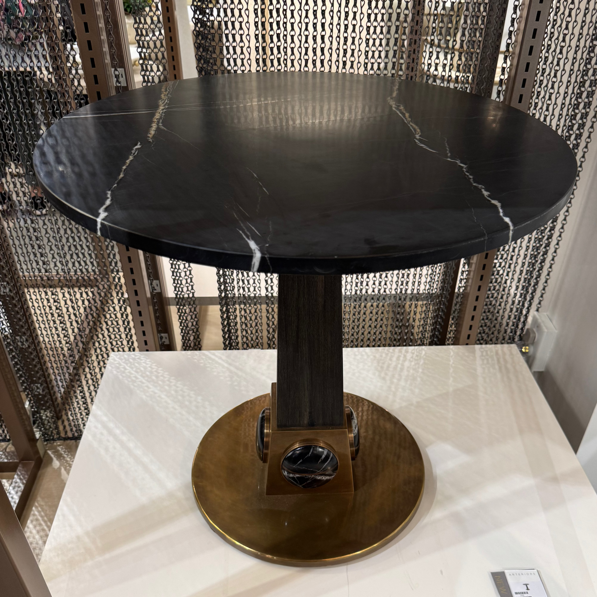 Round black marble table on a white marble base with a textured wall in the background