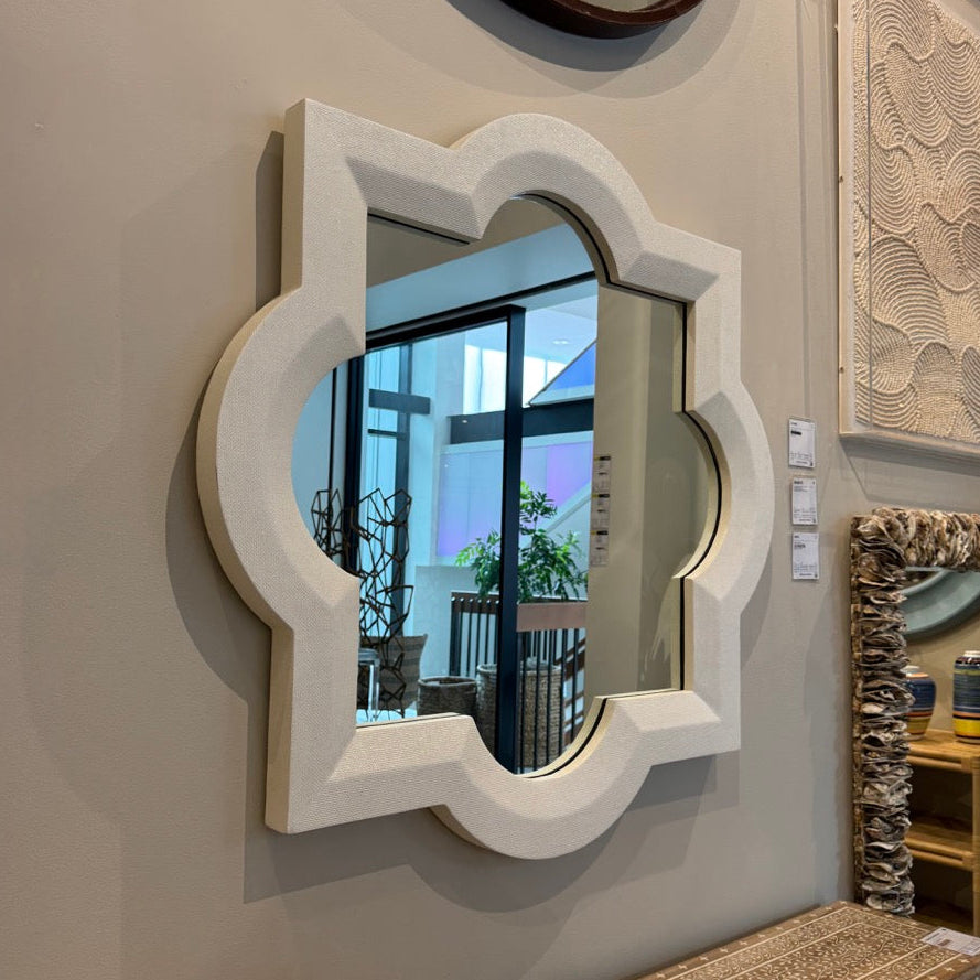 Decorative wall mirror with intricate white frame on a light gray wall.