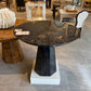 Round black dining table with a white pedestal base in a showroom setting.