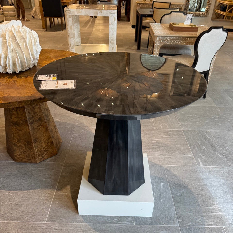 Round black dining table with a white pedestal base in a showroom setting.