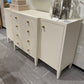 White dresser with gold knobs in a room setting with a mirror and decorative items.