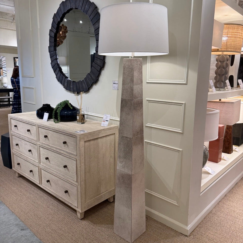 Furniture store interior with a dresser, mirror, and tall lamp.