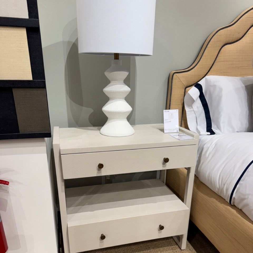 White nightstand with a lamp next to a bed in a bedroom setting